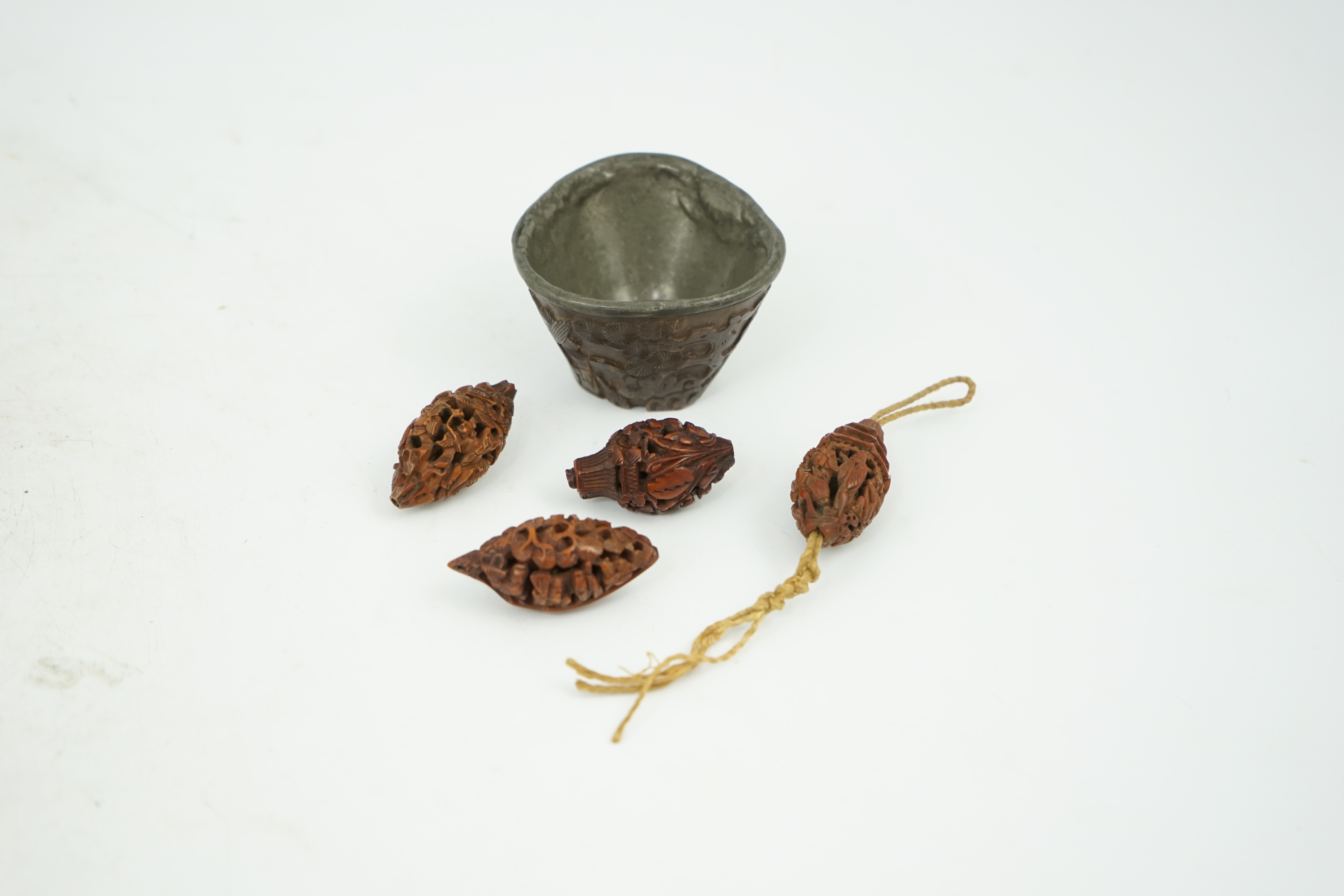 Four Chinese carved peach stones and an 18th/19th century Chinese carved wood cup, 6cm wide (5). Condition - fair to good